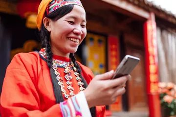 A cheerful woman in traditional clothing using her smartphone during a festive moment, showing how easily the 26JLPH app fits into everyday life.