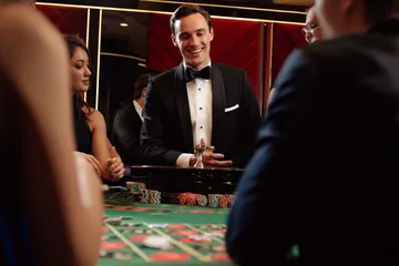 A professional dealer in a tuxedo greeting players at the roulette table, symbolizing the authentic live casino feel at 26JLPH.