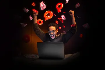 A man celebrating a winning moment on his laptop while gaming symbols float around him, capturing the excitement of 26JLPH games.